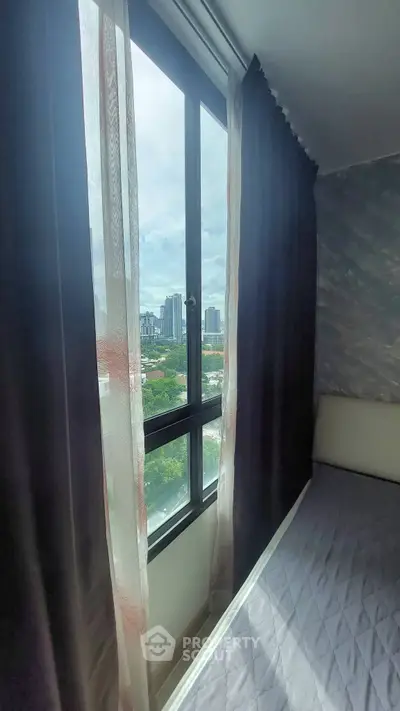 Cozy bedroom with large window offering stunning cityscape views, perfect for urban living.