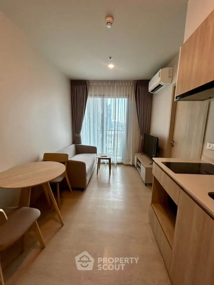 Modern living room with cozy furniture and natural light, featuring a compact dining area and sleek kitchen.