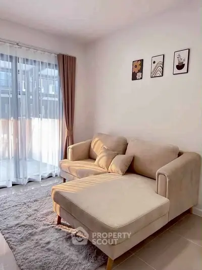 Cozy living room with beige sofa and natural light through large windows.
