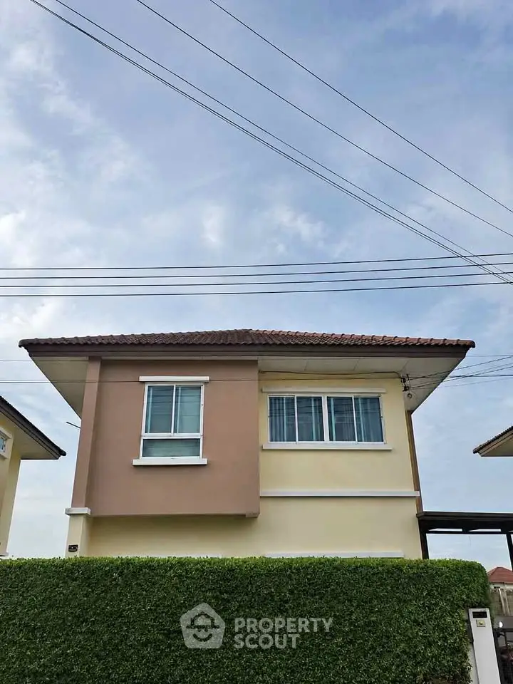 Charming two-story house with a tiled roof and lush green hedge, perfect for family living.
