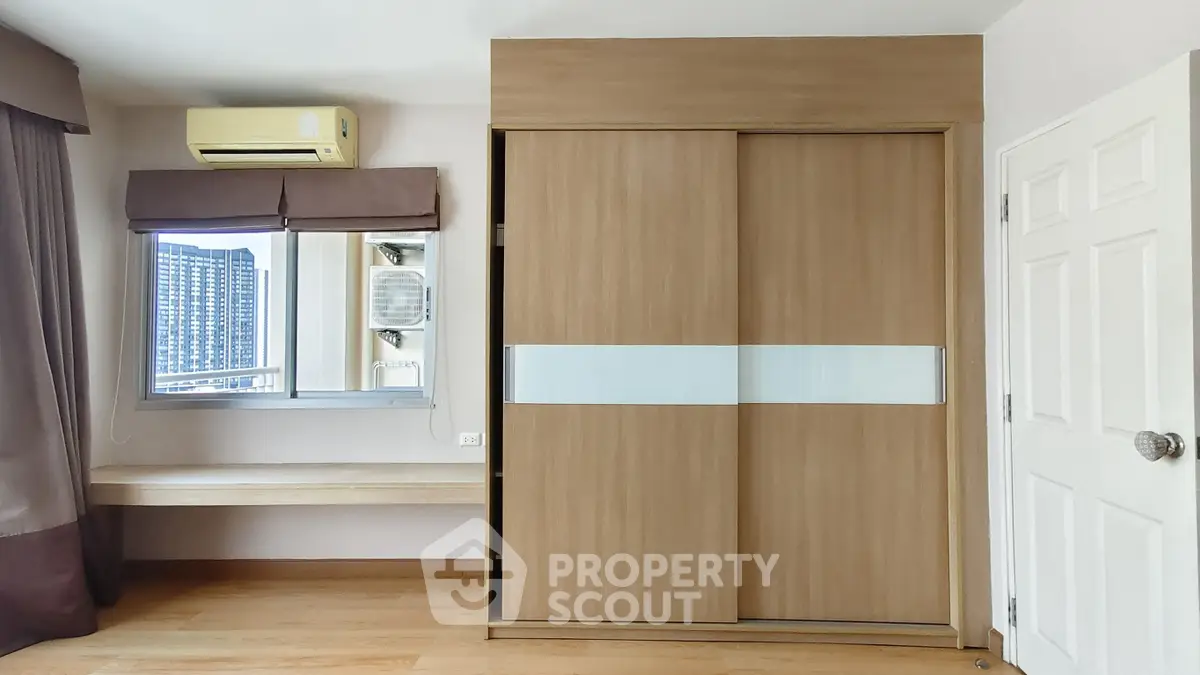 Modern bedroom with built-in wardrobe and city view window, featuring sleek wooden finishes and air conditioning.