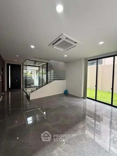 Spacious modern living room with glass staircase and garden view, perfect for contemporary living.