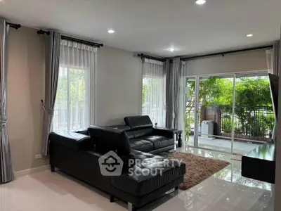 Spacious living room with modern black leather sofas and large windows opening to a lush garden view.