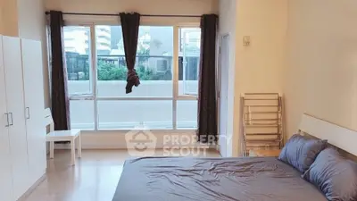 Spacious bedroom with large windows and modern furnishings in urban apartment.