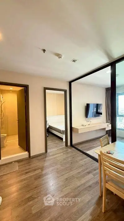 Modern apartment interior with open living area and bedroom, featuring sleek wooden flooring and contemporary design.