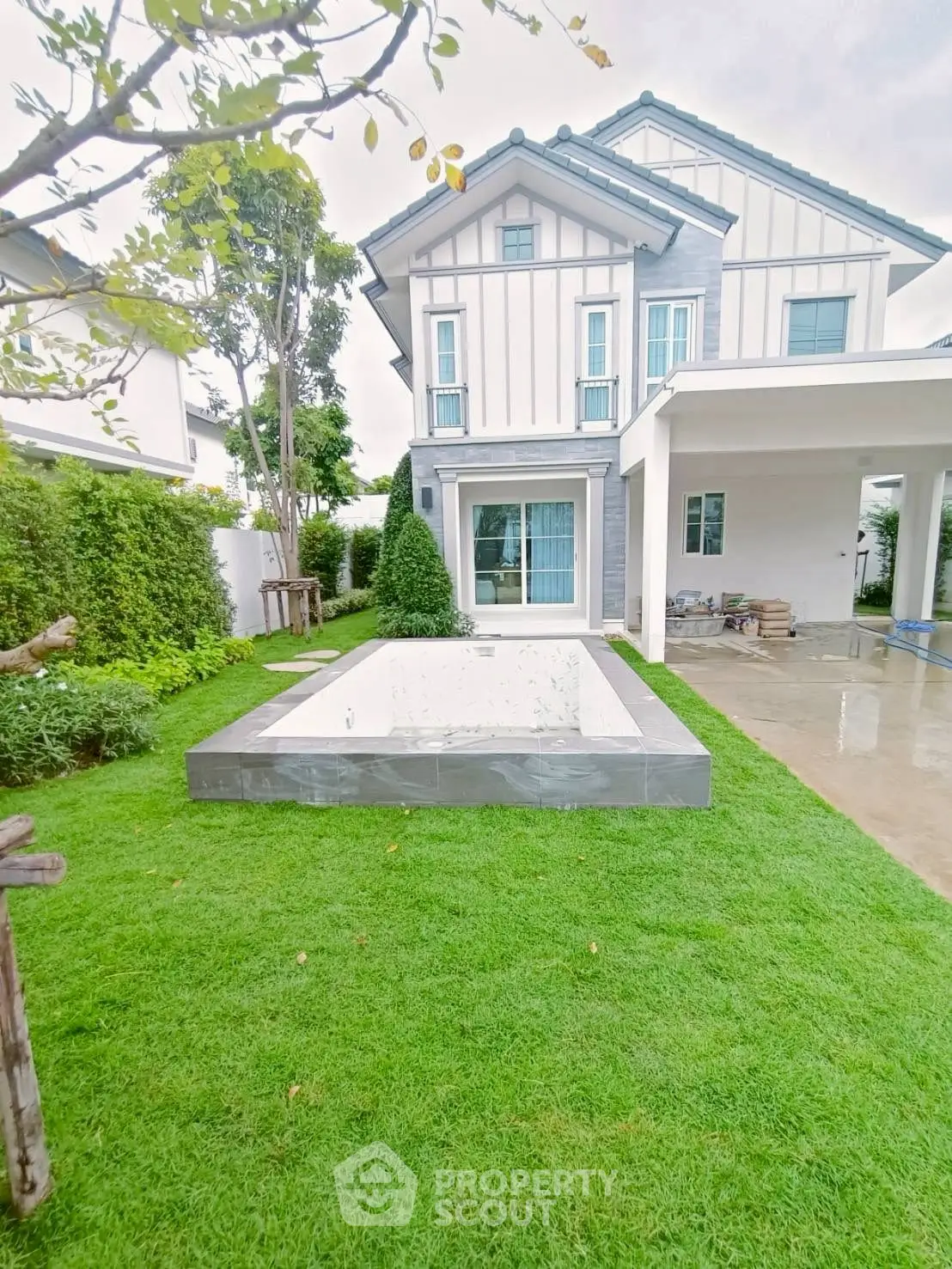 Charming suburban home with lush green lawn and unfinished pool in backyard