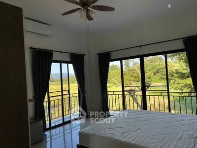 Bright bedroom with large windows offering stunning natural views and ceiling fan.