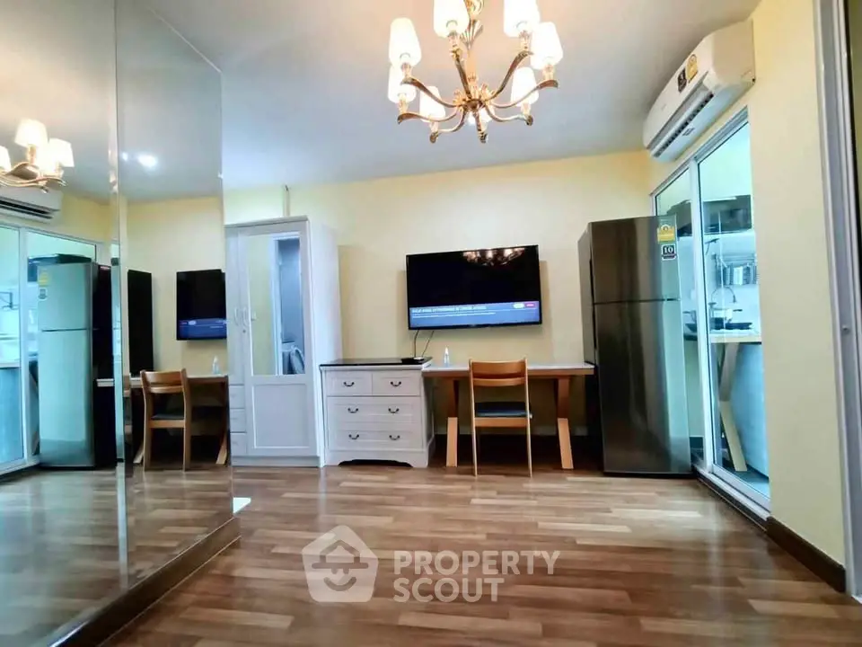 Modern living room with wooden flooring, chandelier, and mirrored wall for spacious feel.