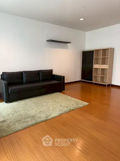 Spacious living room with sleek black sofa and modern shelving unit on wooden flooring.
