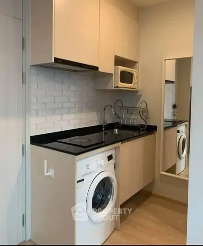 Modern compact kitchen with washing machine and microwave in stylish apartment.