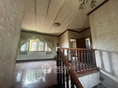 Spacious vintage living area with wooden staircase and large windows, offering a classic charm and natural light.