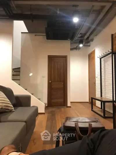 Modern living room with stylish decor and wooden flooring, featuring a cozy sofa and contemporary lighting.