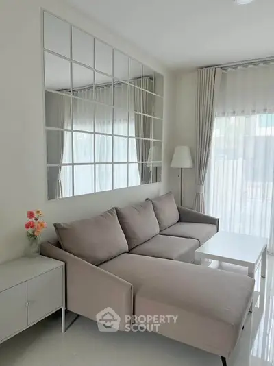 Modern living room with stylish gray sofa, large mirror, and natural light from floor-to-ceiling windows.