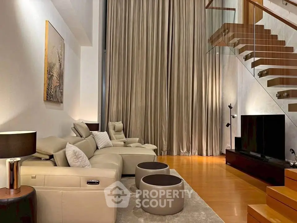 Luxurious modern living room with high ceilings, elegant staircase, and plush leather seating.