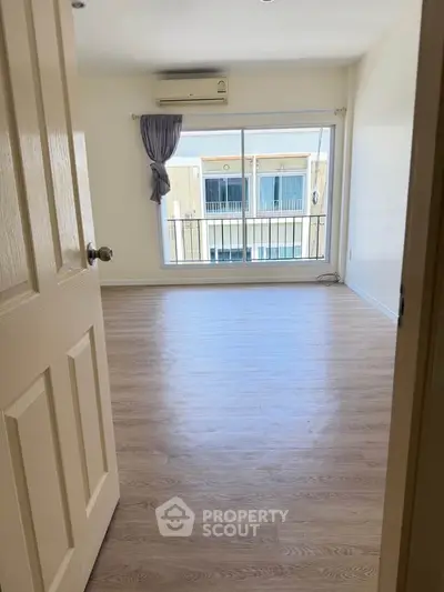 Spacious bedroom with wooden flooring and large window offering natural light.