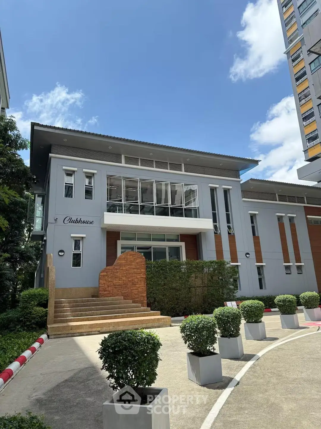 Modern clubhouse exterior with sleek design and lush greenery in a residential complex.