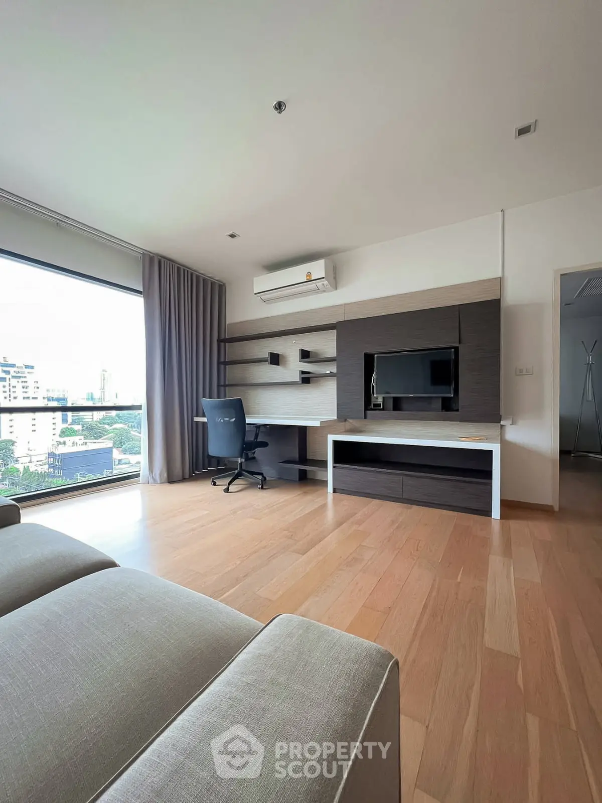 Spacious modern living room with large window and built-in desk, offering a stunning city view.