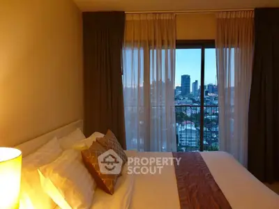 Cozy bedroom with city view from large window, featuring elegant curtains and plush bedding.