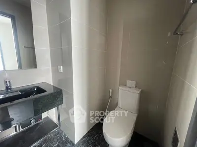 Modern bathroom with sleek black sink and white toilet in a compact space.