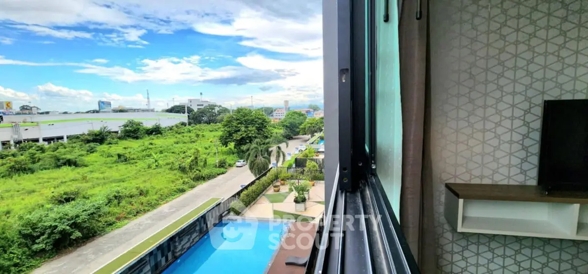 Stunning view from modern apartment window overlooking lush greenery and pool