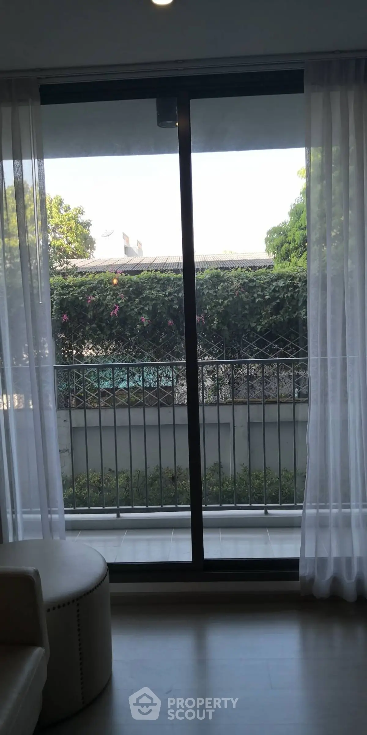 Charming balcony view with lush greenery and natural light through sliding glass doors.