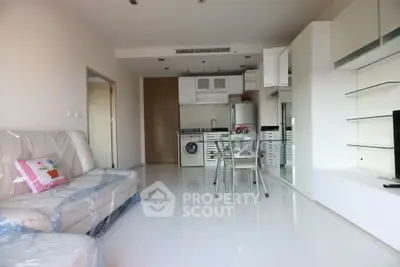 Modern open-plan living room with kitchen, featuring sleek furniture and bright white flooring.