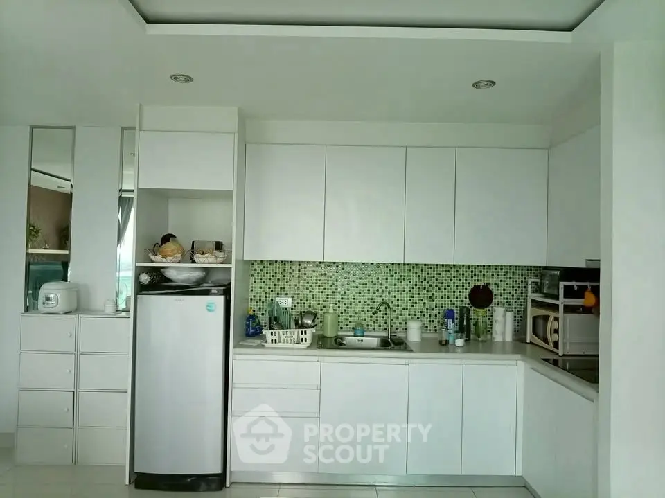 Modern kitchen with sleek white cabinets and green mosaic backsplash, featuring a compact fridge and microwave.