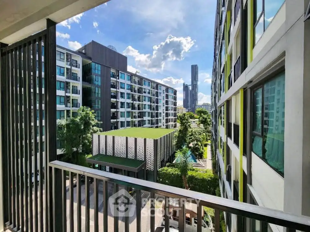 Modern apartment complex with lush greenery and city skyline view from balcony.