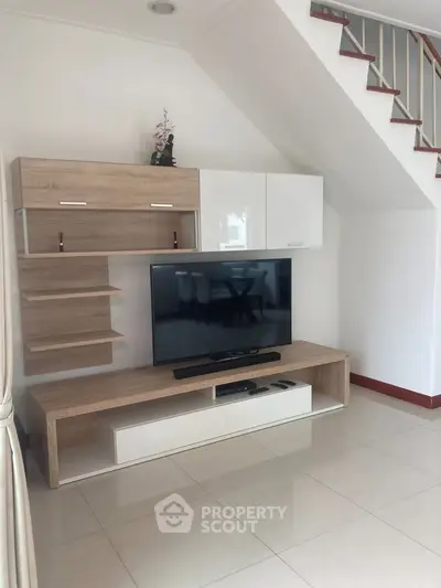 Modern living room with sleek TV unit and stylish shelving under staircase