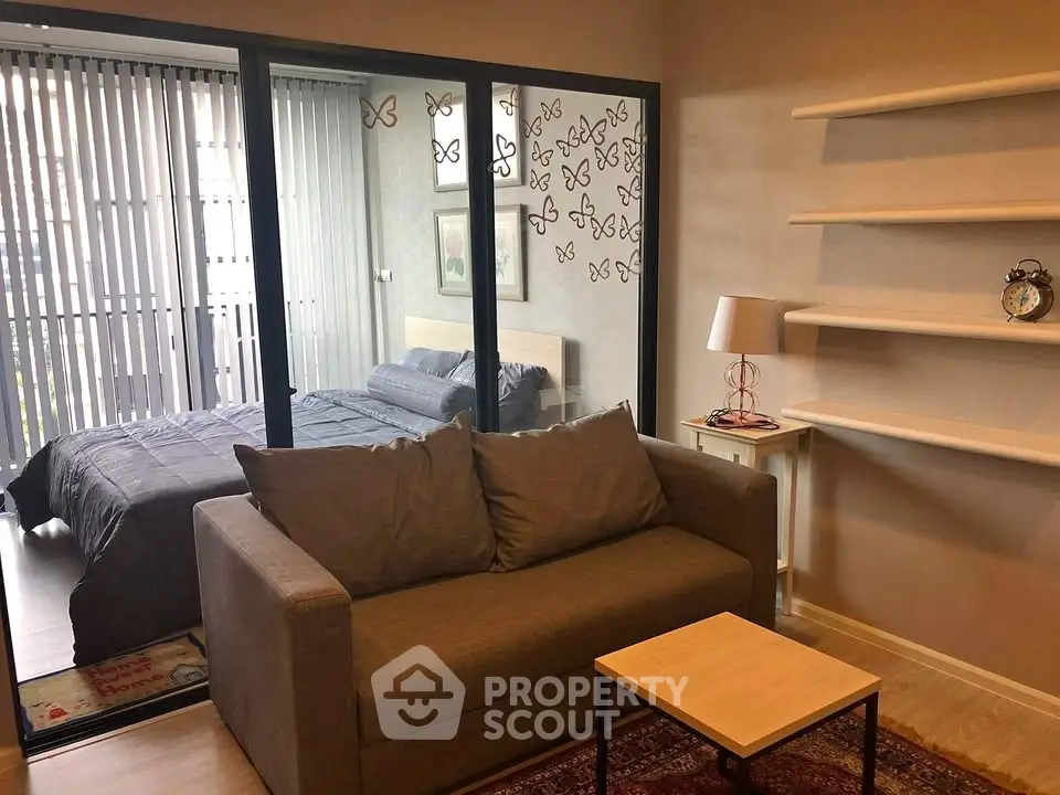 Modern living room with cozy sofa and view into stylish bedroom through glass partition.