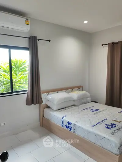 Cozy bedroom with natural light and air conditioning, featuring a comfortable bed and neutral decor.