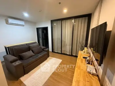 Modern living room with sleek furniture and wooden flooring, featuring a cozy sofa and large TV.
