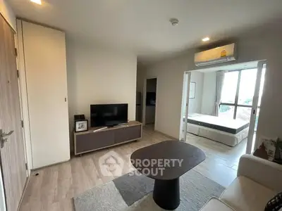Modern living room with sleek furniture and a view into a cozy bedroom, featuring natural light and stylish decor.