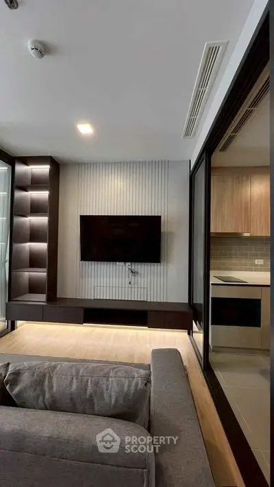 Modern living room with sleek TV setup and open kitchen view, featuring contemporary design and stylish furnishings.