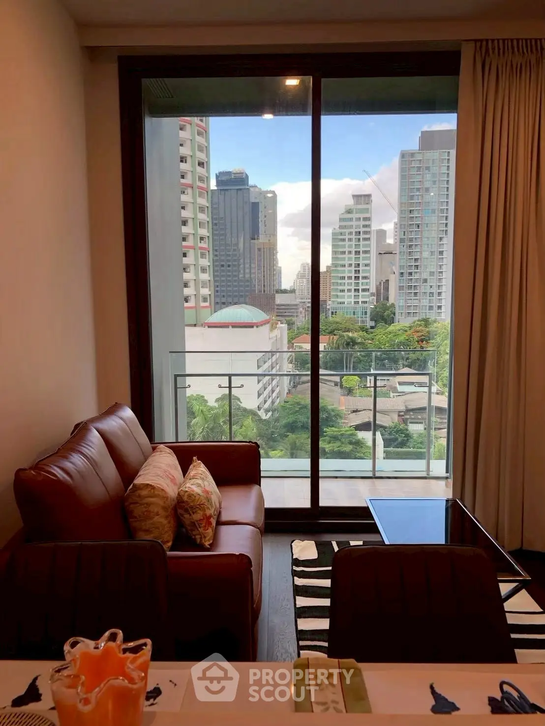 Modern living room with city view from large window, featuring stylish furniture and cozy ambiance.