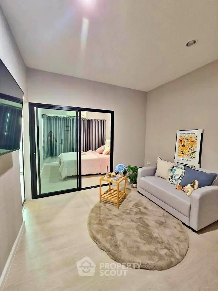 Modern living room with cozy sofa and view into stylish bedroom through glass doors.