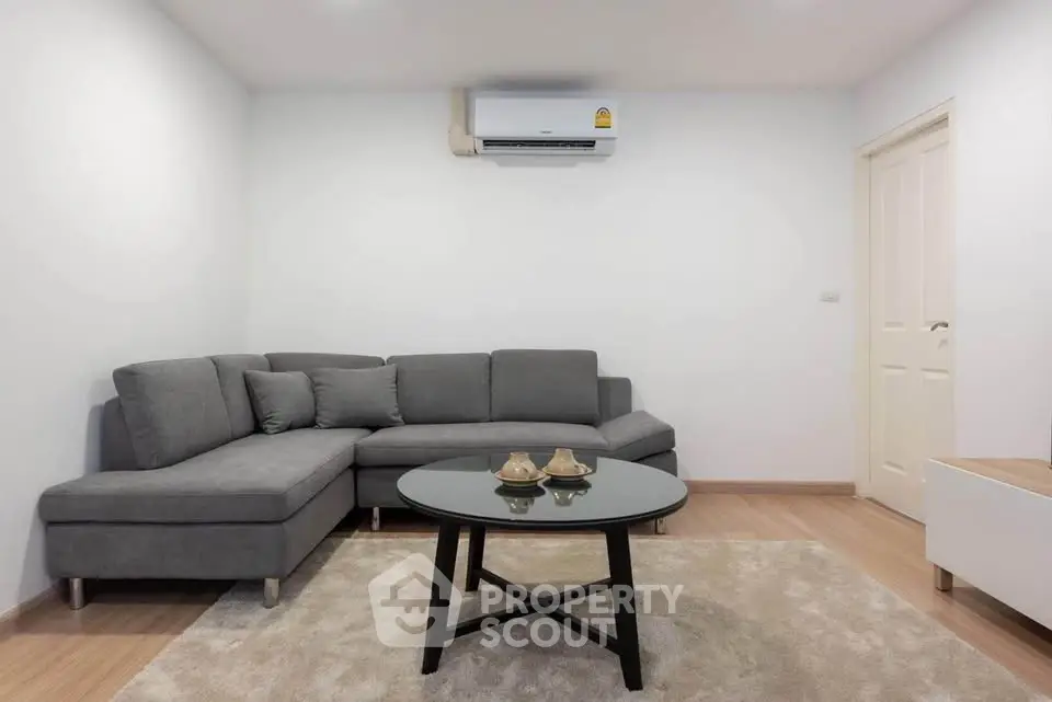Modern living room with gray sectional sofa and round coffee table on plush rug.
