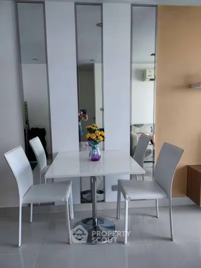 Modern dining area with sleek white chairs and table, accented by a vibrant flower centerpiece.