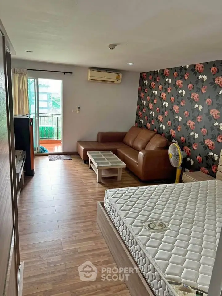 Spacious living room with floral accent wall, leather sofa, and balcony access in modern apartment.