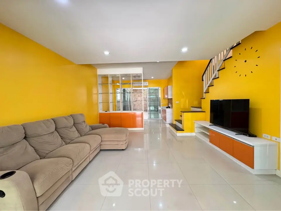Spacious living room with vibrant yellow walls, modern staircase, and cozy seating area.