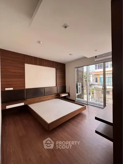 Spacious bedroom with modern wooden flooring and large windows for natural light.