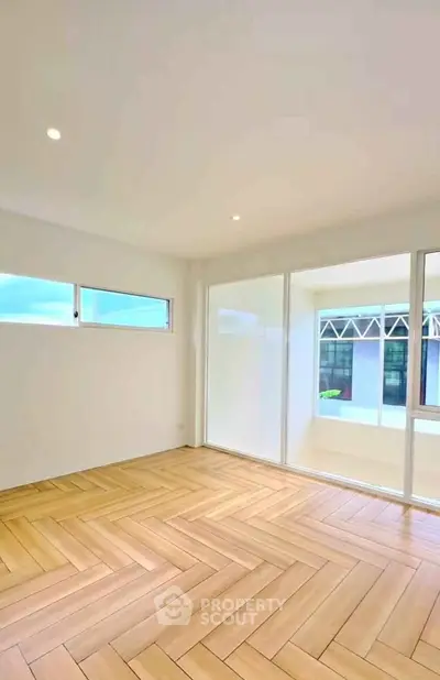 Spacious empty room with elegant wooden flooring and large windows for natural light.