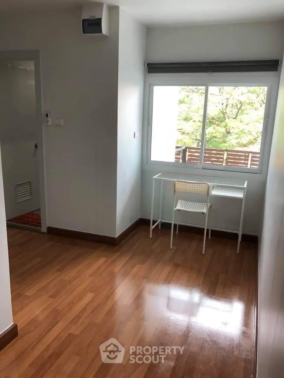 Bright room with wooden flooring and a window view, featuring a small desk and chair.