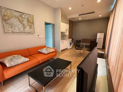 Modern living room with vibrant orange sofa and open kitchen layout, featuring a washing machine and stylish decor.