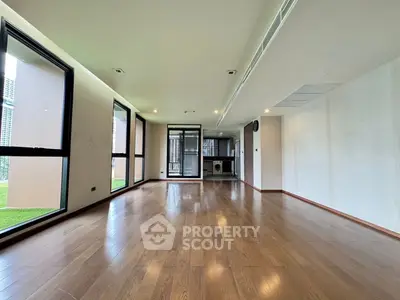 Spacious modern living room with hardwood floors and large windows in a luxury apartment.