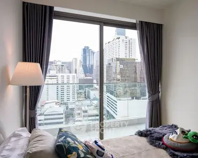Modern bedroom with city view from large window, featuring cozy decor and stylish curtains.