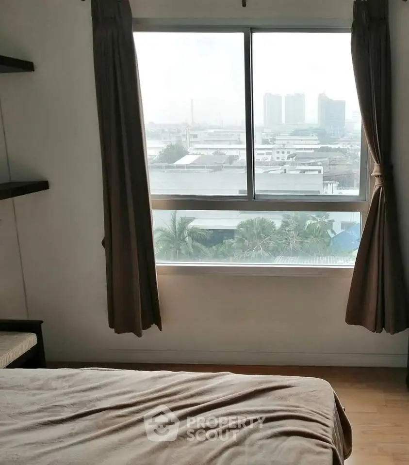 Cozy bedroom with city view through large window, perfect for urban living.