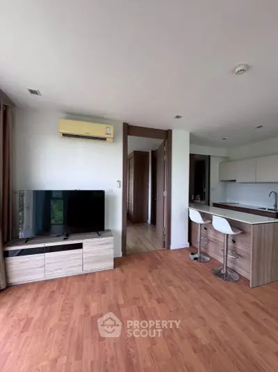 Modern open-plan living room with kitchen, featuring wood flooring and stylish bar seating.