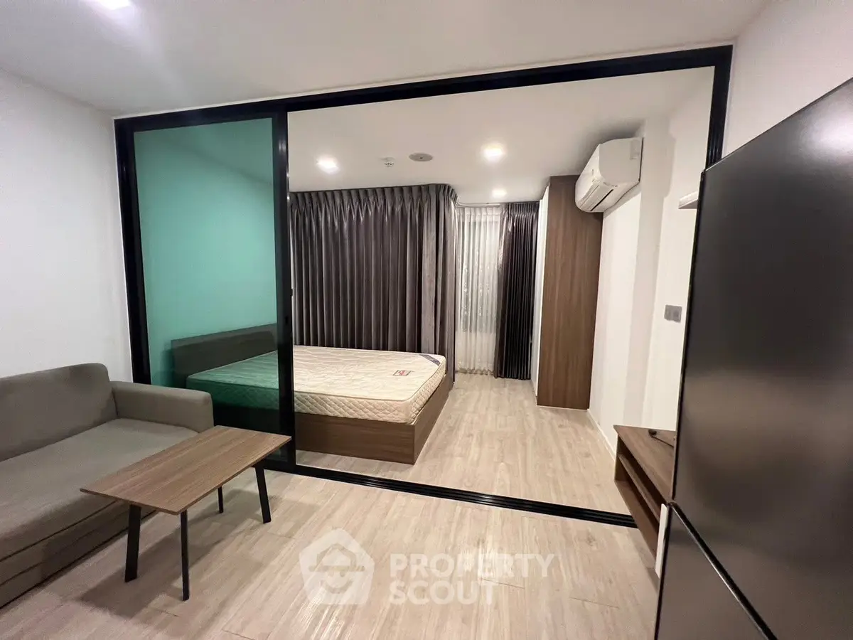 Modern studio apartment with sliding glass partition, cozy living area, and air-conditioned bedroom.