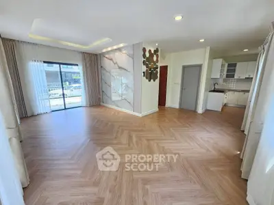 Spacious open-plan living room with elegant wood flooring and modern kitchen area.